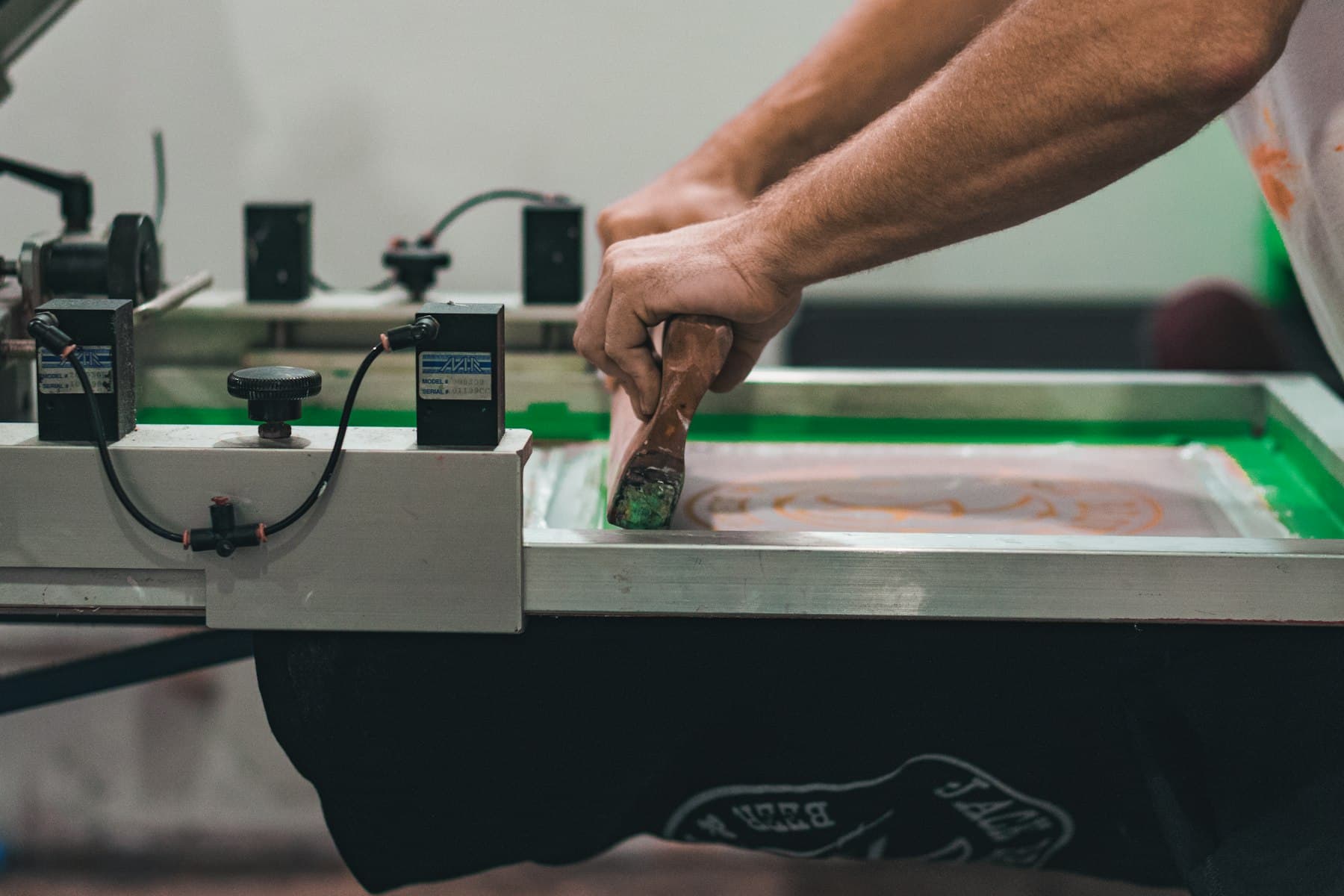 Screen printing press operator pulling ink across a screen in a print shop